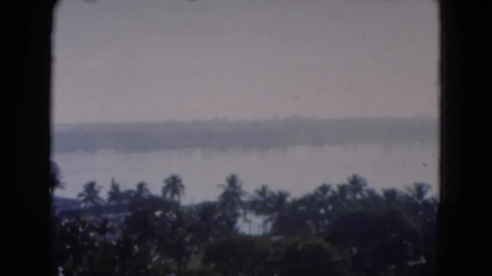 1975 Florida 8mm frame showing a soft, hazy coastal landscape through dark window framing, with palms and water beyond.