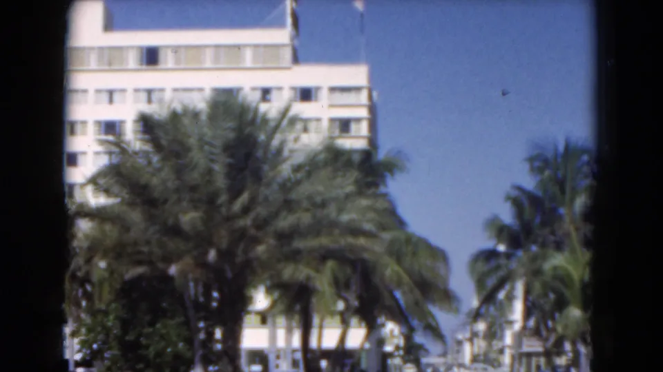 Palm trees frame a sunlit pale building in Florida, seen in soft 8mm home-movie footage.
