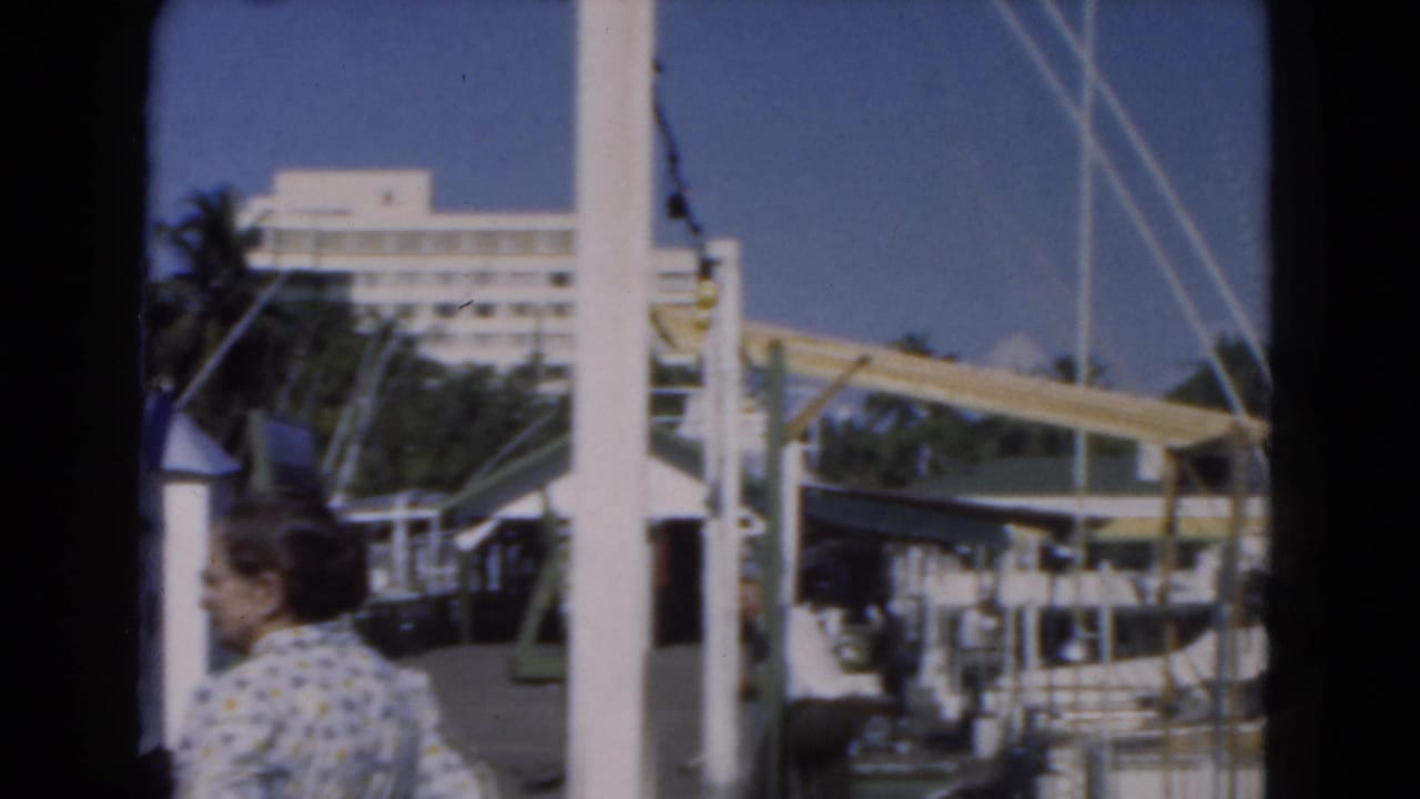 A woman walks past docked boats and masts at a sunny marina.