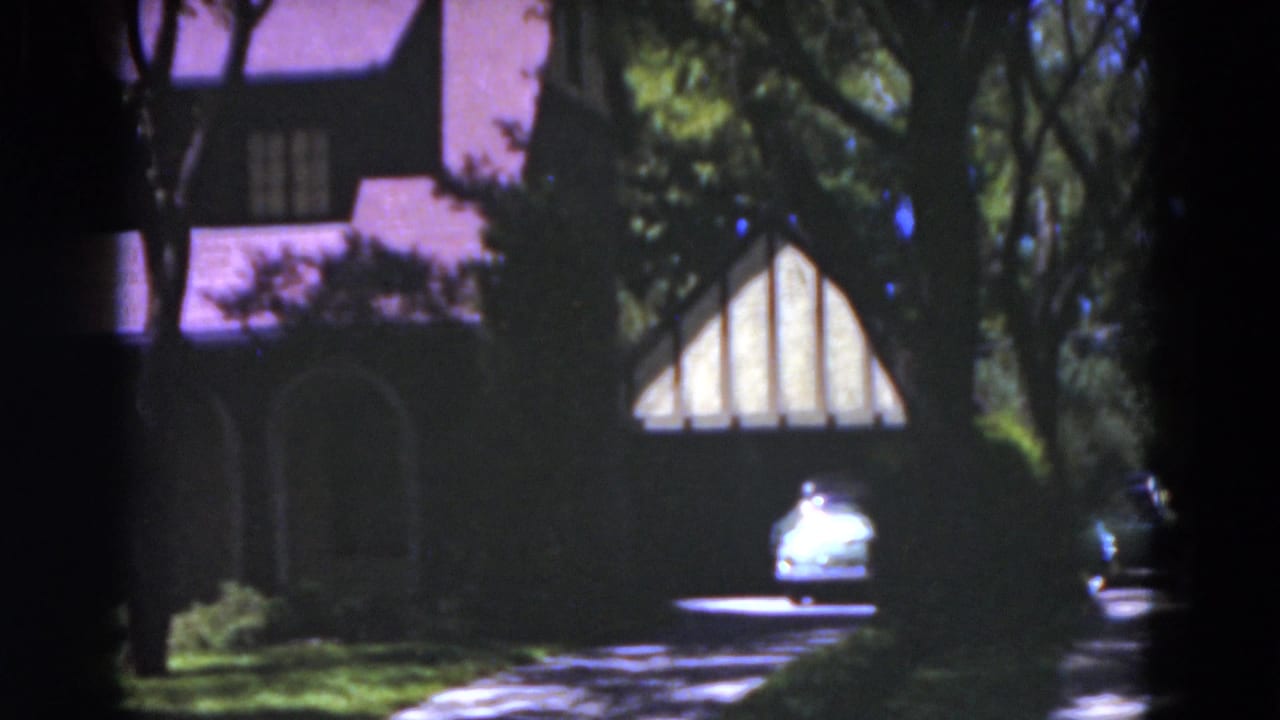 Tudor-style house partly shaded by trees with a car in the driveway.