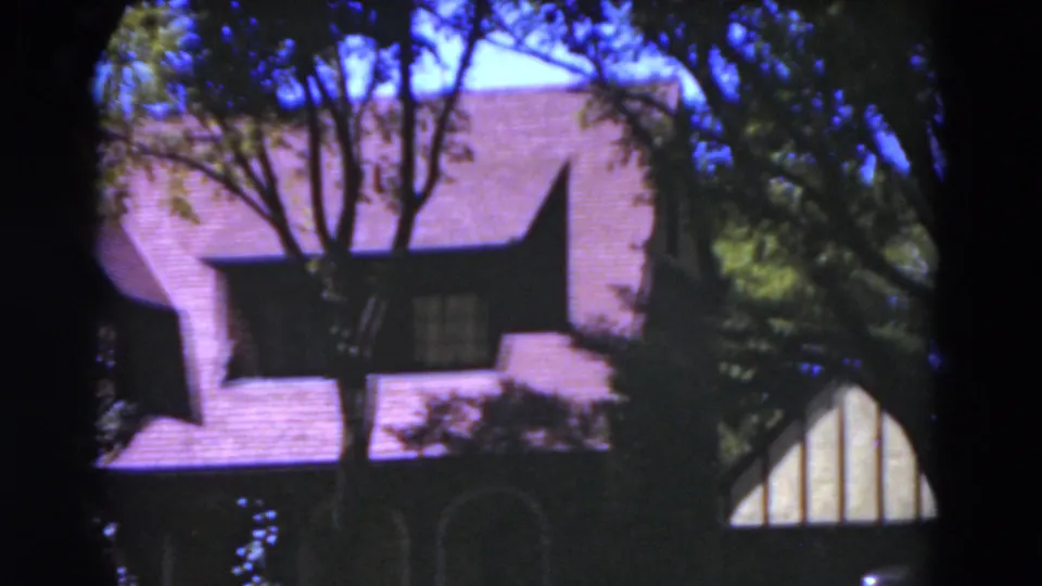 1975 Florida 8mm frame showing rooflines, arched openings, and tree cover on a Tudor-style residence.