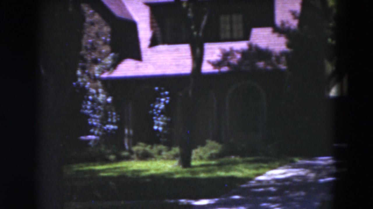Large shadowed house with lawn, trees and a driveway in front.