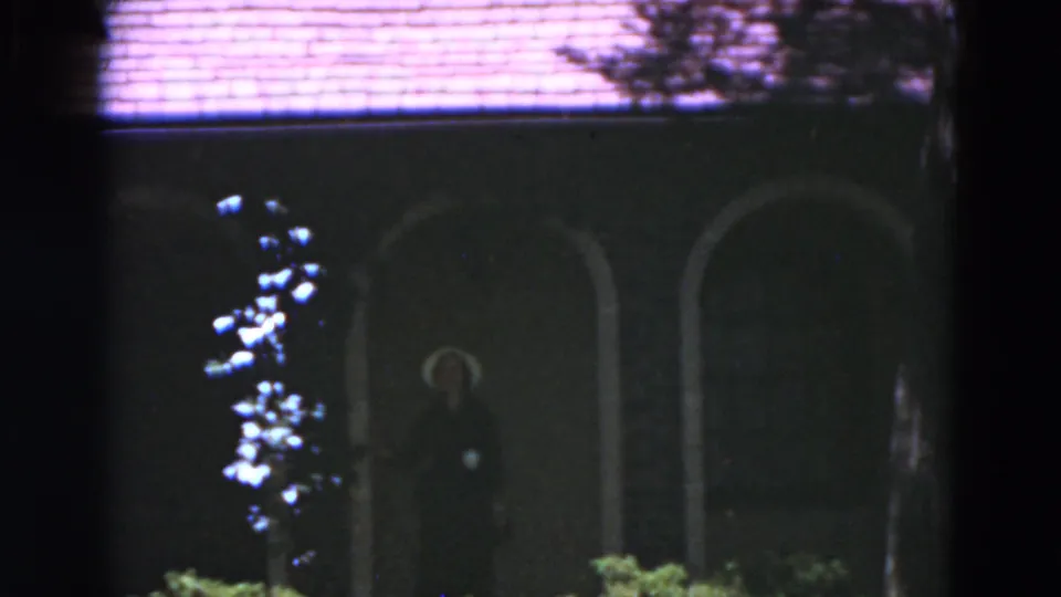 1975 Florida 8mm frame showing a woman in a light hat standing in the dark arched entry of a large house.