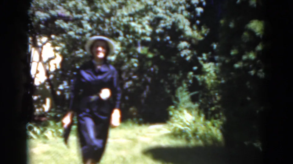 A closer 1975 home-movie frame shows the woman smiling slightly while walking through the leafy Florida garden.