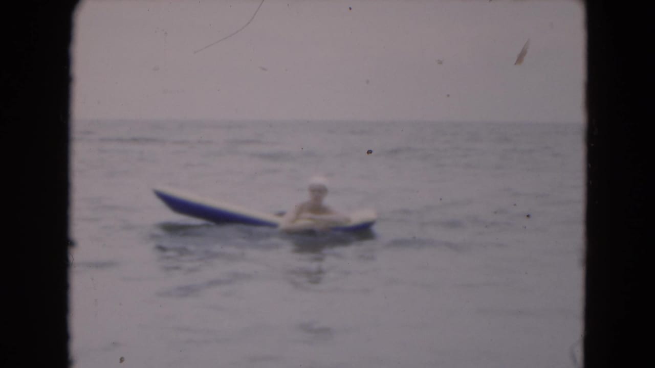 Woman on a raft drifting across calm water under a pale sky.