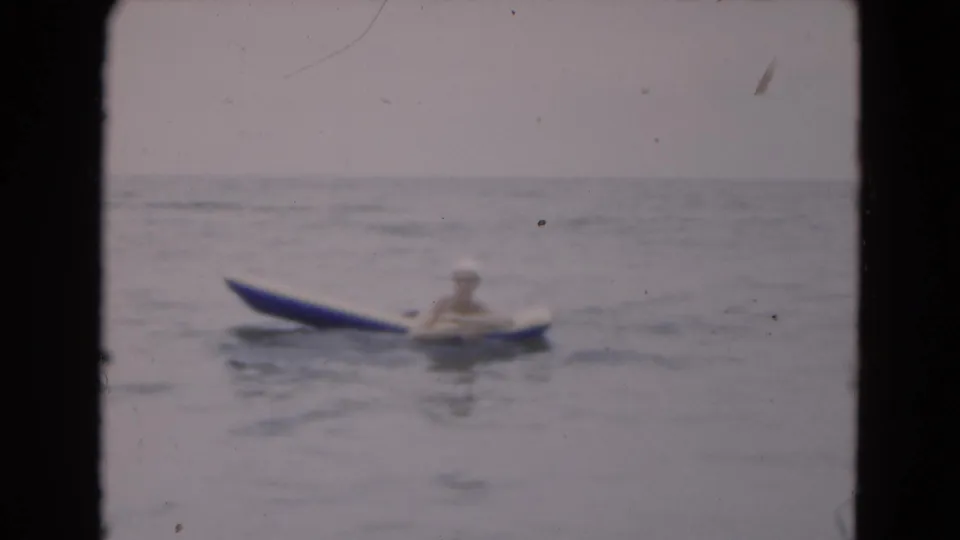 The woman remains on the raft in calm Florida ocean water, seen through soft, faded 8mm color.