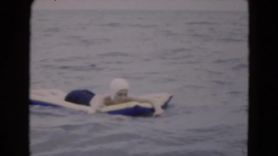 Closer 1975 Florida home-movie view of the woman paddling on the raft, with her swim cap and face area more visible.
