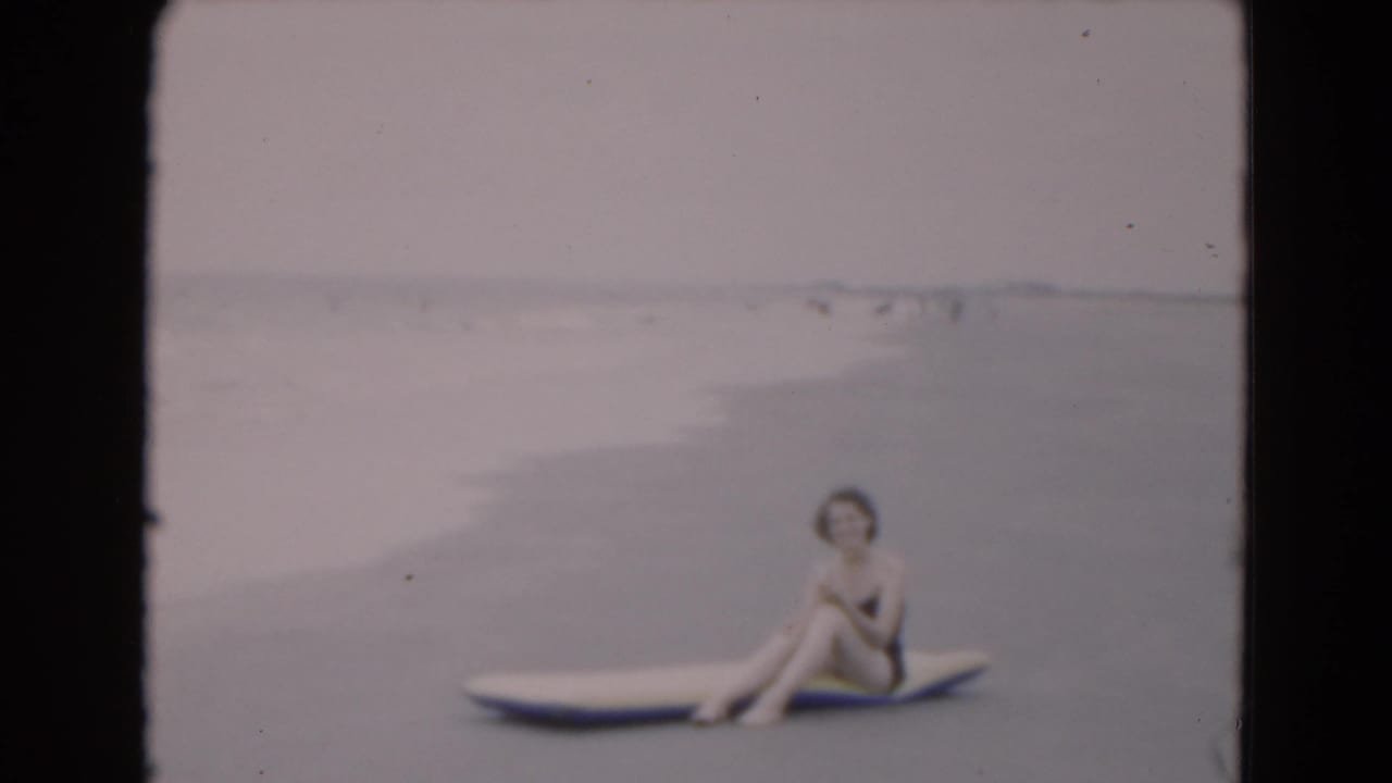 Woman in a dark swimsuit sits on an inflatable raft near the shoreline.
