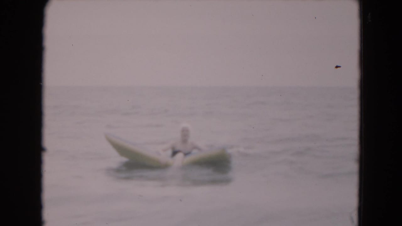 Person seated on an inflatable raft in calm ocean water under a pale sky.
