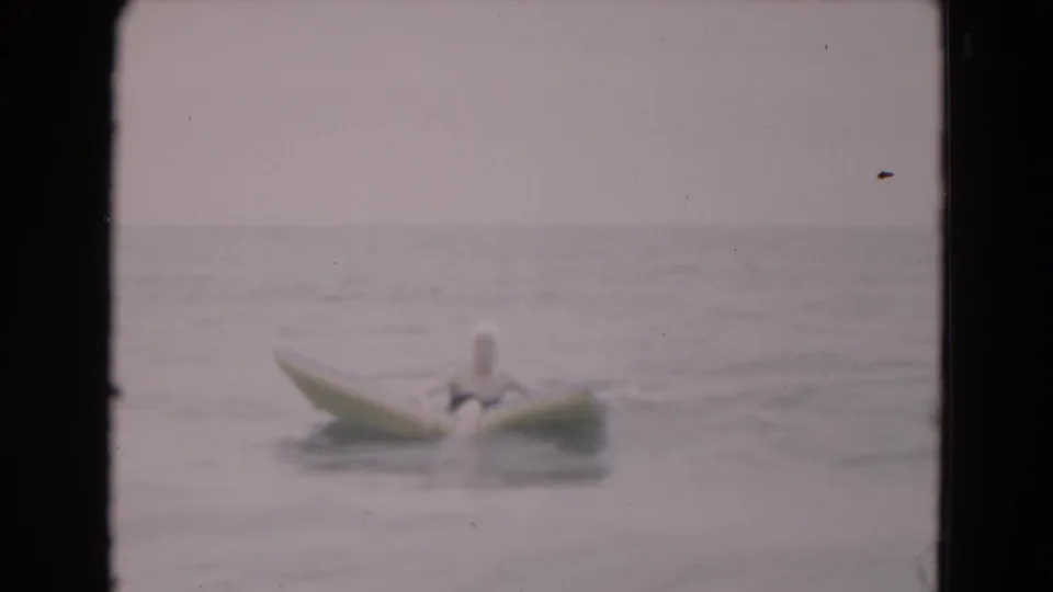 1975 Florida 8mm frame showing a person on a yellow inflatable raft floating in soft, gray ocean water.
