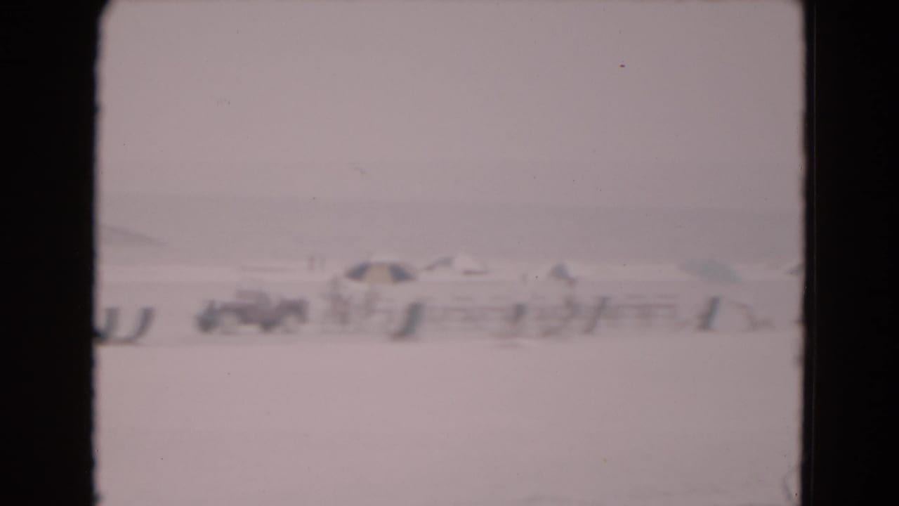 Distant low structures on a pale icy landscape, framed by dark 8mm film borders.