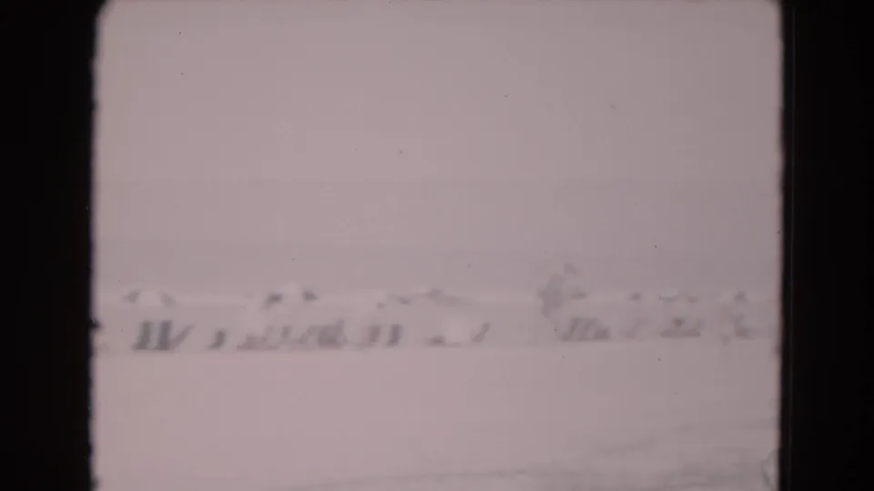 Soft 1975 8mm Florida frame showing a washed-out snowy or frost-like exterior with low distant structures and a gray sky.