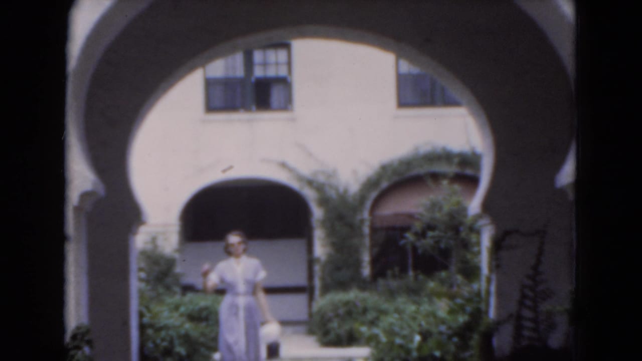 Woman in a pale dress standing under white stucco arches with greenery behind her.