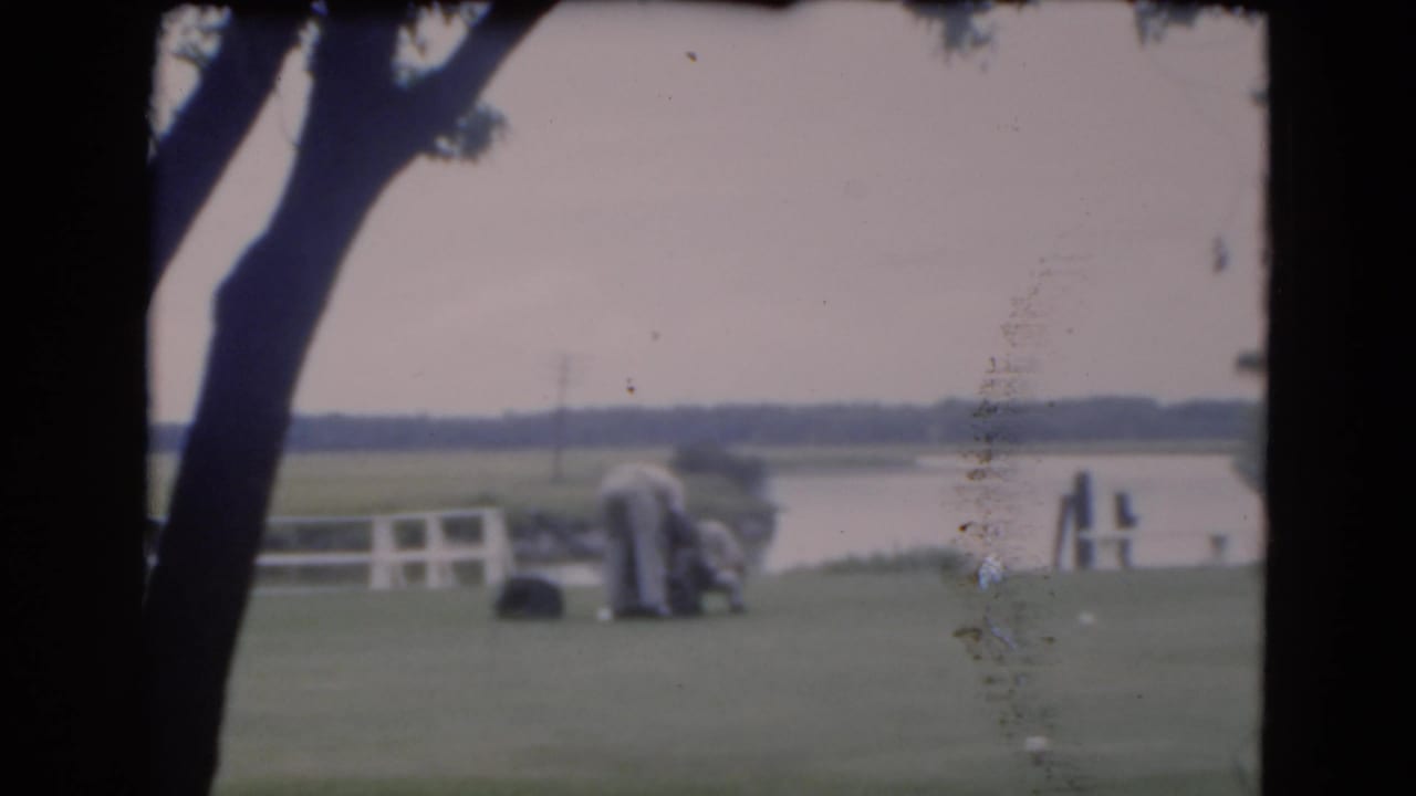 Distant men on a lawn by a waterway with trees framing the scene.