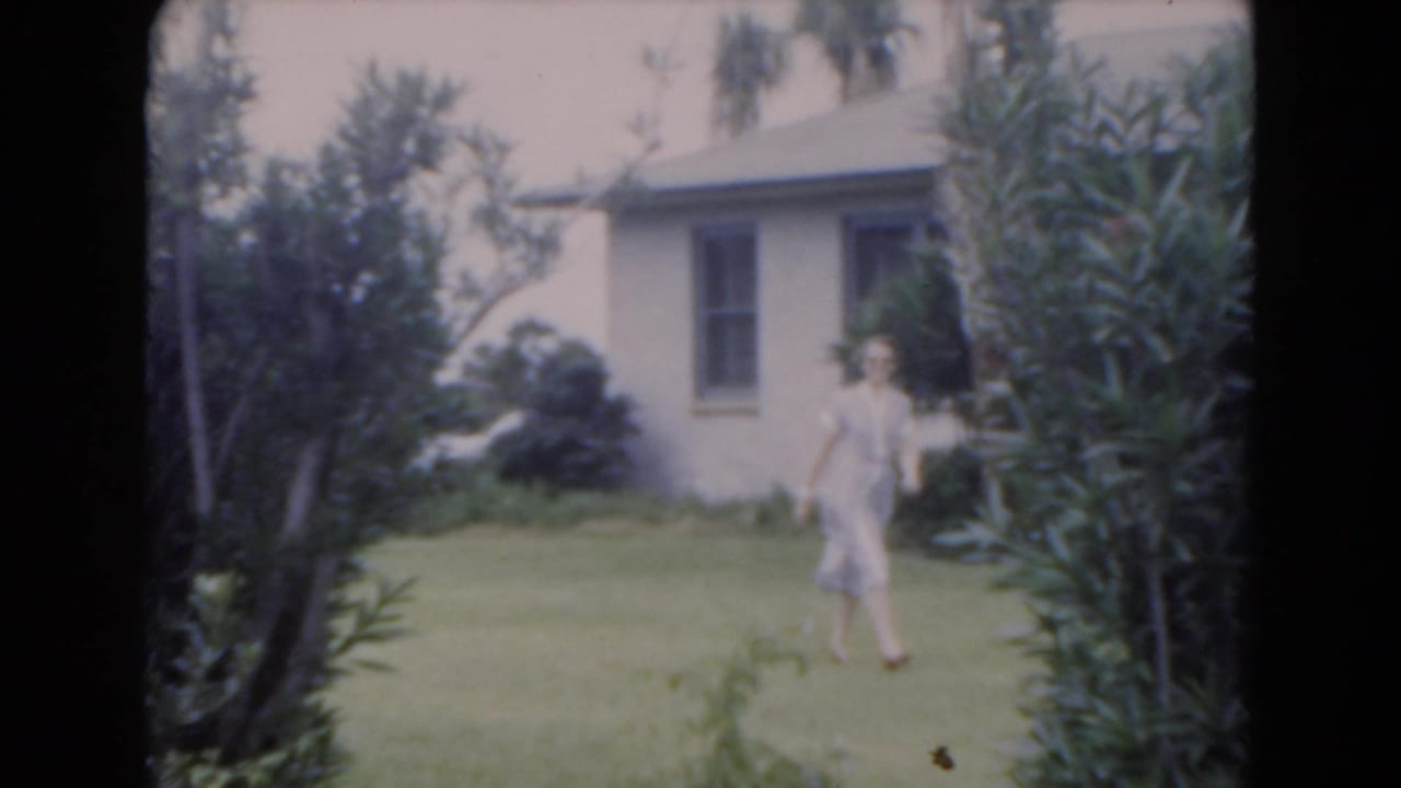 Woman in a light dress walks across a lawn near a house.