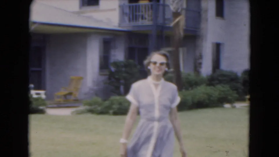Close 1975 Florida home-movie frame of an adult woman in sunglasses and a light dress facing the camera on a lawn.