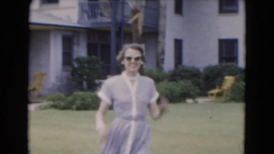 In 1975 Florida home-movie footage, a young woman in sunglasses and a light dress walks across a lawn toward the camera.
