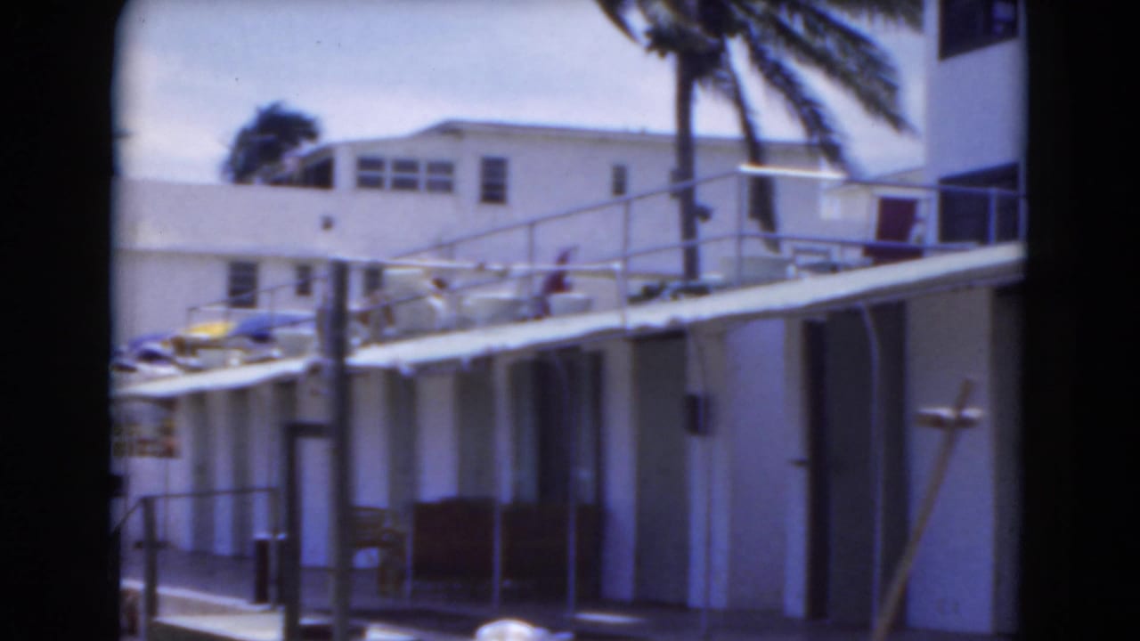 White beachside villas with railings, umbrellas, palms, and sand in front.