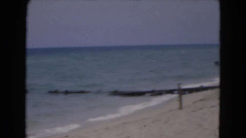1975 Florida beach view with soft ocean surf, sand, wooden posts, and black 8mm projection borders.