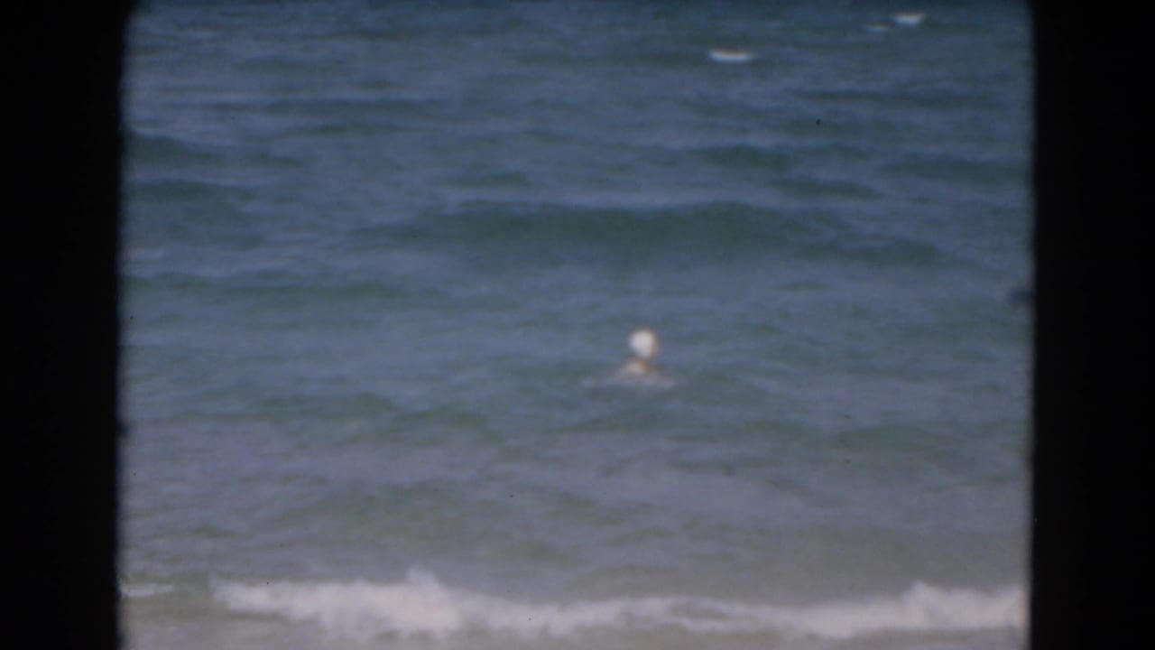 Distant swimmer bobbing in blue-green ocean waves behind dark foreground edges.