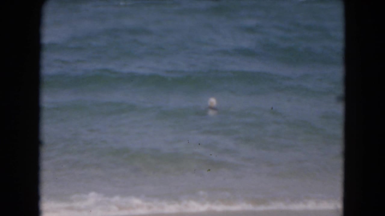 A distant swimmer appears in rolling Florida surf in this soft, grainy 1975 8mm home-movie frame.