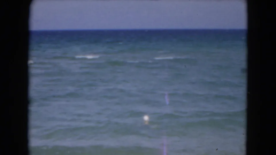 A wide 1975 Florida 8mm view shows the ocean horizon and a small swimmer low in the frame amid gentle waves.