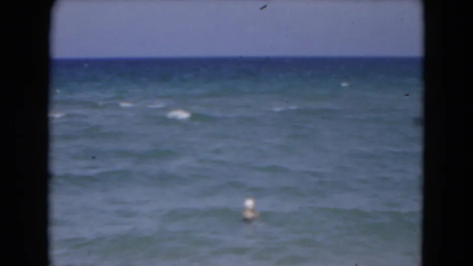 1975 Florida 8mm home-movie frame showing open ocean, low waves, pale sky, and a small white buoy offshore.