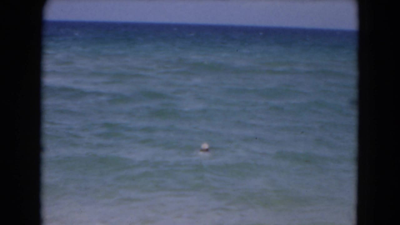 1975 Florida coastal home-movie frame with blue-green water, faint surf texture, pale sky, and a buoy offshore.
