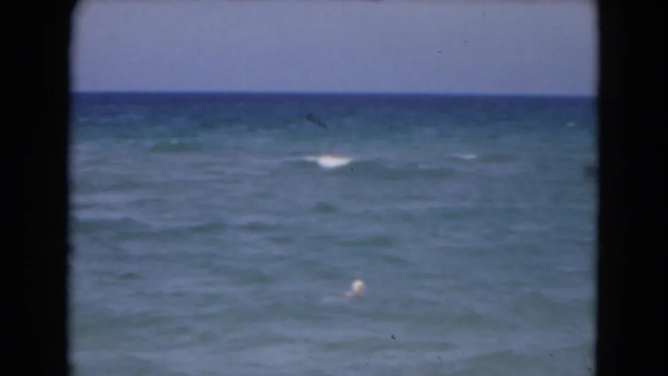 1975 Florida 8mm frame showing open water, a white buoy, soft surf movement, and dark home-movie borders.