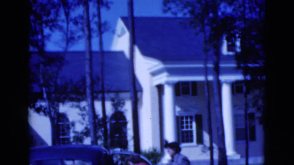 1975 Florida frame with two women beside a parked car, seen against a white columned house and trees.