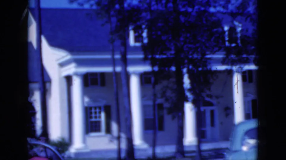 1975 Florida frame showing the columned house through trees as the front of a car appears at the lower right.