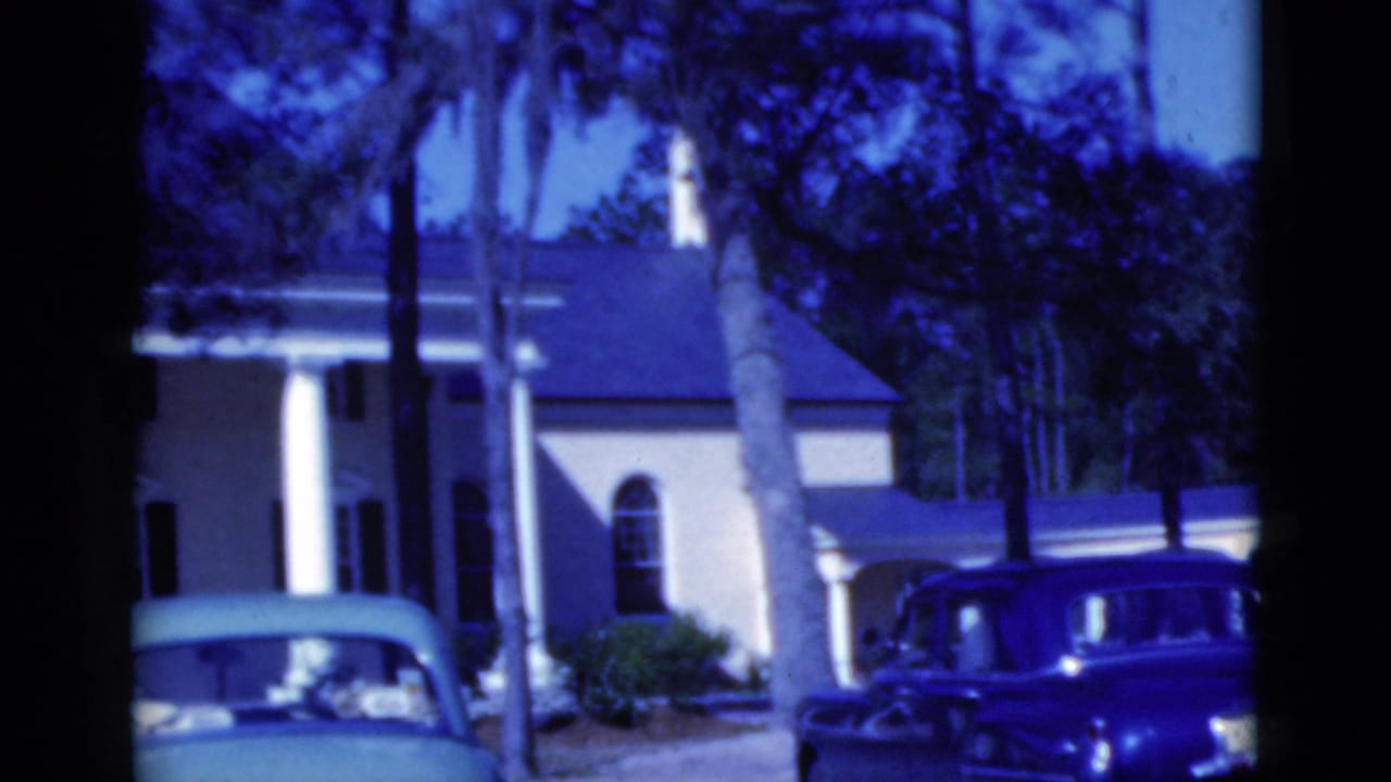 Large house with white columns, palms, and two parked vintage cars.