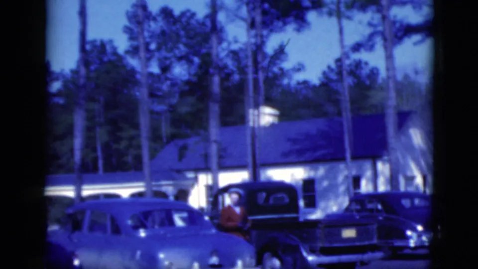 1975 Florida 8mm still showing parked cars, a dark pickup, and a person in a red shirt near the vehicle at dusk.