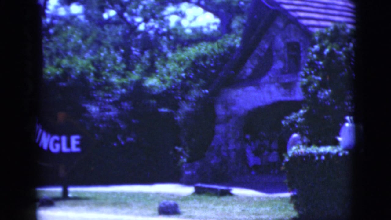 Entrance sign partly cropped as the frame shifts toward the stone building and roof.