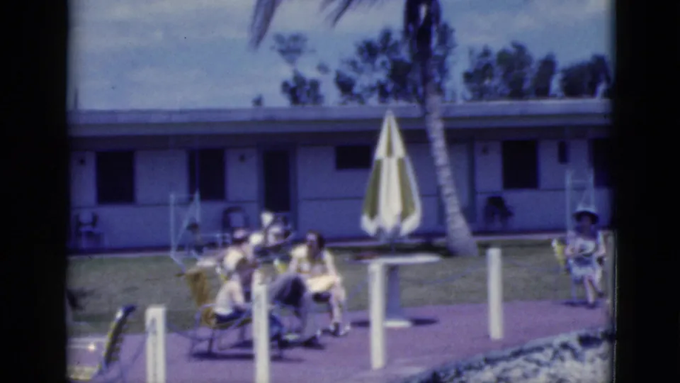 1975 Florida poolside view with adults sunning in lounge chairs, a striped umbrella, palm tree, lawn, and motel-style building.