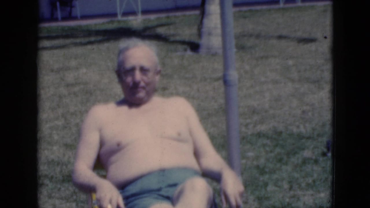 An older man in green swim trunks sits in a striped lawn chair on a sunny lawn, consistent with the supplied 1975 Florida vacation metadata.