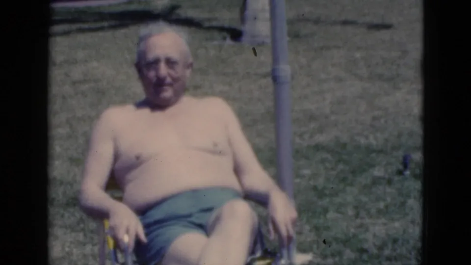 The older man remains seated outdoors in a lawn chair, looking toward the camera in soft 8mm 1970s Florida vacation footage.