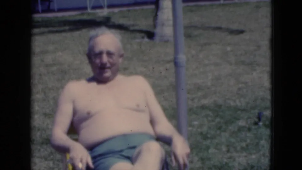 An older man sits back in a striped lawn chair on grass, part of a brief 1975 Florida home-movie vacation scene.