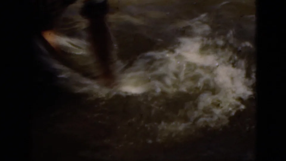 Close 1975 Florida 8mm frame of splashing pond water with a dark pole partly visible during the alligator-handling sequence.