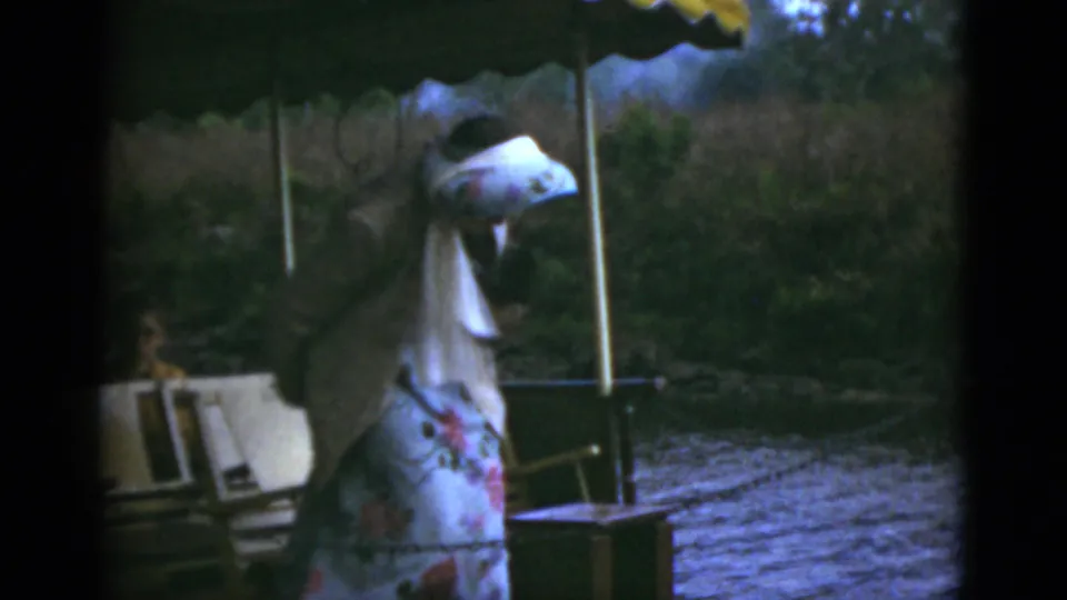 In 1975 Florida home-movie footage, a woman in a hat and light clothing adjusts herself on a covered riverboat deck.