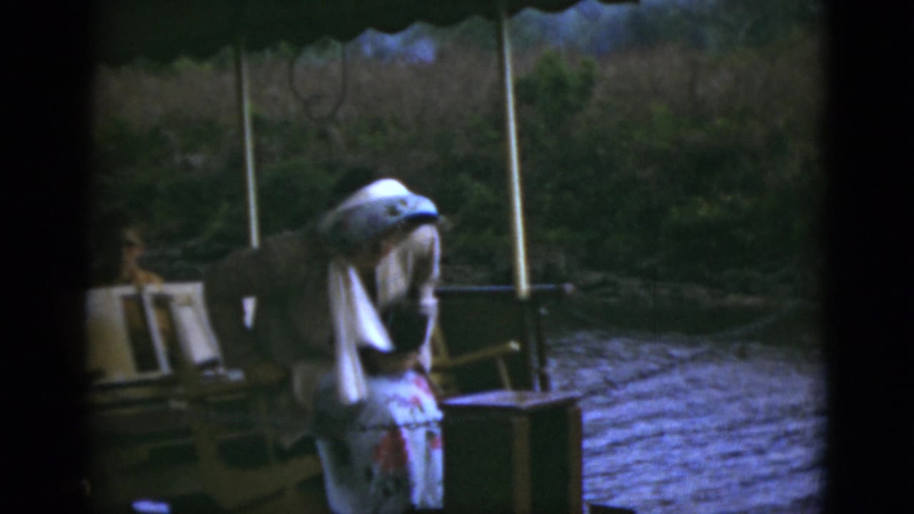 Woman bends forward on a boat deck beside chairs and river water.