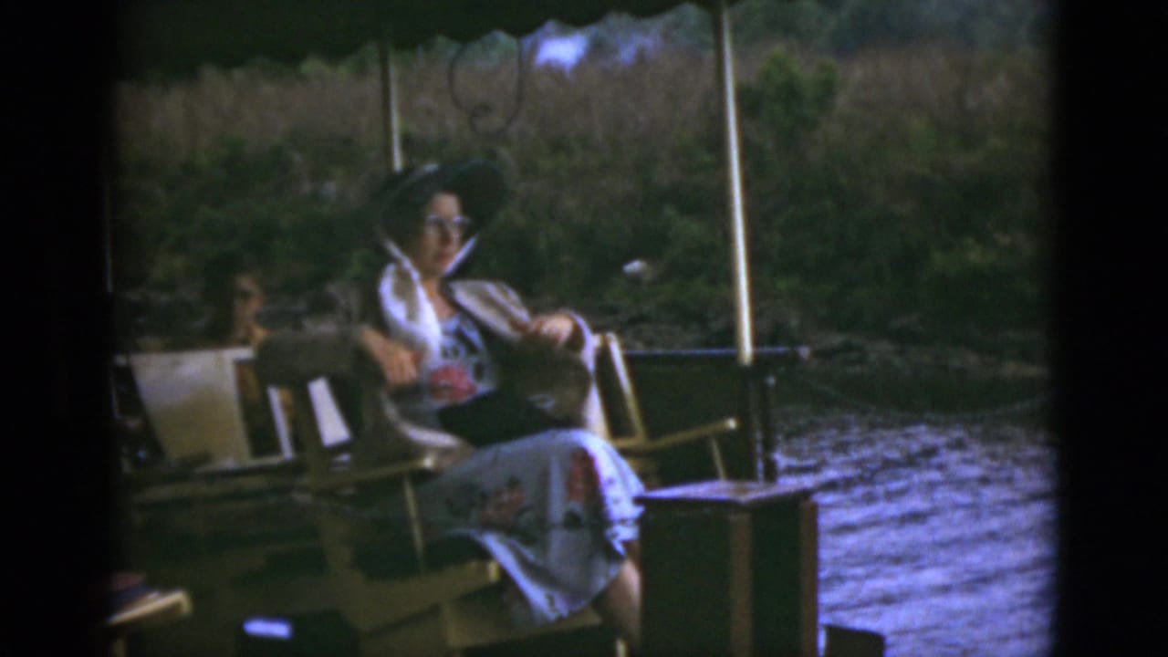 Woman seated on a boat deck near water and shoreline vegetation.