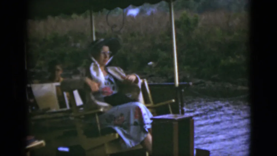 A woman relaxes on the deck of a small boat in 1975 Florida home-movie footage, with water and greenery behind her.
