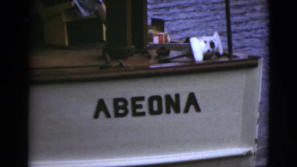 Close view of a boat surface bearing the name Abeona, with deck objects and a brick or stone wall nearby.