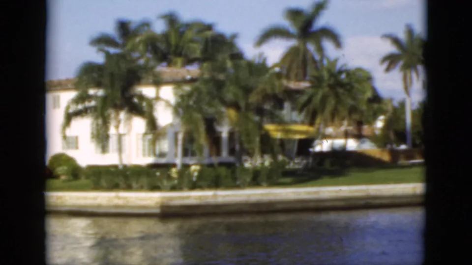 A waterfront residence with palm trees, lawn, seawall, and canal water appears in the 1975 Florida boat-cruise footage.