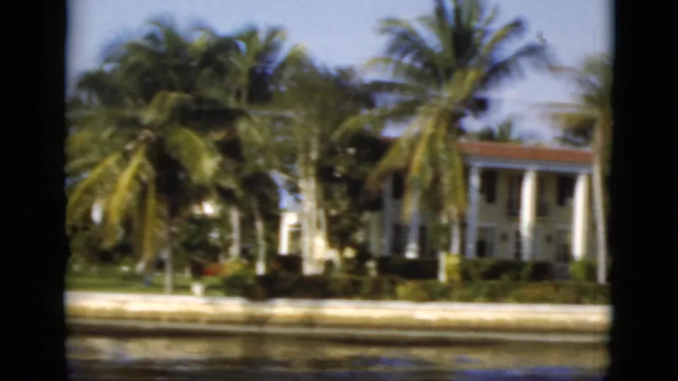 1975 Florida home-movie view of palm trees, a seawall, and large waterfront houses seen from a boat.