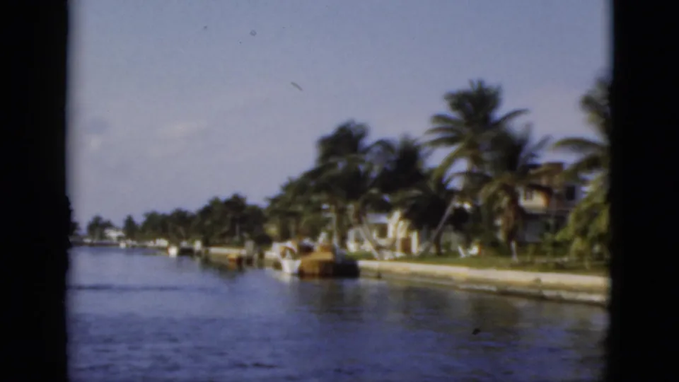 Boat-level 1975 Florida view down a calm canal with palm trees, docks, seawalls, and waterfront residences.