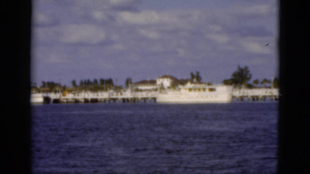 White boat beside a long dock across blue water under a cloudy sky.