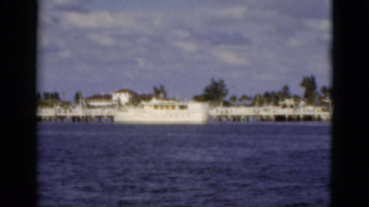 Waterfront dock and white boat seen across calm water with trees behind.