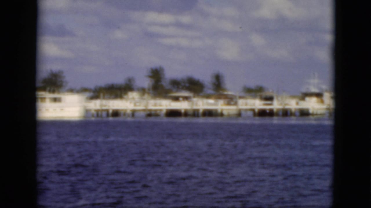 Waterfront pier with docked boats across blue water under a cloudy sky.